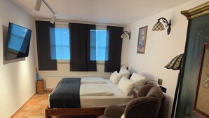 Ein Schlafzimmer mit einem Bett, einem Sessel, einem Fernseher und einem Fenster mit Jalousien.