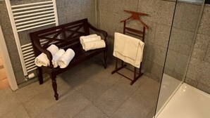 Ein Badezimmer mit einer Sitzbank, einem Handtuchhalter und einer Duschkabine aus Glas.