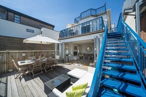 Een terras met buitenmeubilair, een trap en uitzicht op het interieur.
