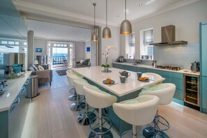 Een moderne keuken met een centraal eiland, barstoelen, hanglampen en uitzicht naar buiten.