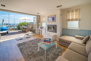 Een moderne woonkamer met een glazen salontafel, een bank, een open haard en uitzicht op de jachthaven.