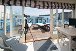 Een balkon met een telescoop, lounge fauteuils, een tafel en uitzicht op zee en boten.