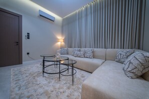 Een moderne woonkamer met een bank, twee ronde tafels, een lamp en een wandairconditioner.