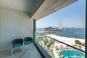 Ein Balkon mit zwei Stühlen, einem Glastisch und Blick auf einen Strand, einen Wasserpark und ein Riesenrad.