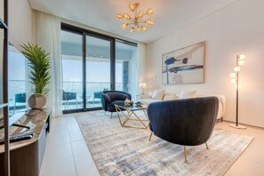 A modern living room with a large window, a black armchair, a coffee table, and a chandelier. - Luxury Sea View 3BR + Maid Apt. at the Address JBR (Dubai)
