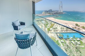 A balcony with two wicker chairs and a small table, overlooking a beach, a pool, and a Ferris wheel. - Luxury Sea View 3BR + Maid Apt. at the Address JBR (Dubai)