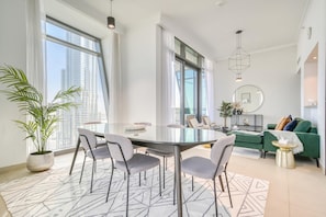 Ein modernes Wohnzimmer mit einem Glastisch, grauen Stühlen, einem grünen Sofa und Blick auf die Stadt.