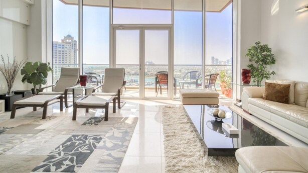 A spacious living room with a large sliding glass door leading to a balcony, furnished with a sofa, chairs, and a coffee table. - Waterfront Sea View Apt w/ Wow Factor on The Palm (Dubai)
