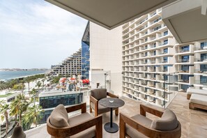 En balkon med havudsigt, et siddeområde med et rundt bord og et reolsystem med forskellige genstande.