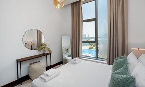 Une chambre d’hôtel avec un grand lit, un miroir rond, une table de chevet avec une lampe, une vue sur la plage et une fenêtre avec des rideaux.