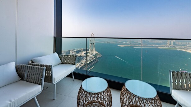A balcony with a view of a bridge and water, furnished with white sofas and round tables. - Gorgeous Apt wz Stunning Sea Views in Address JBR (Dubai)