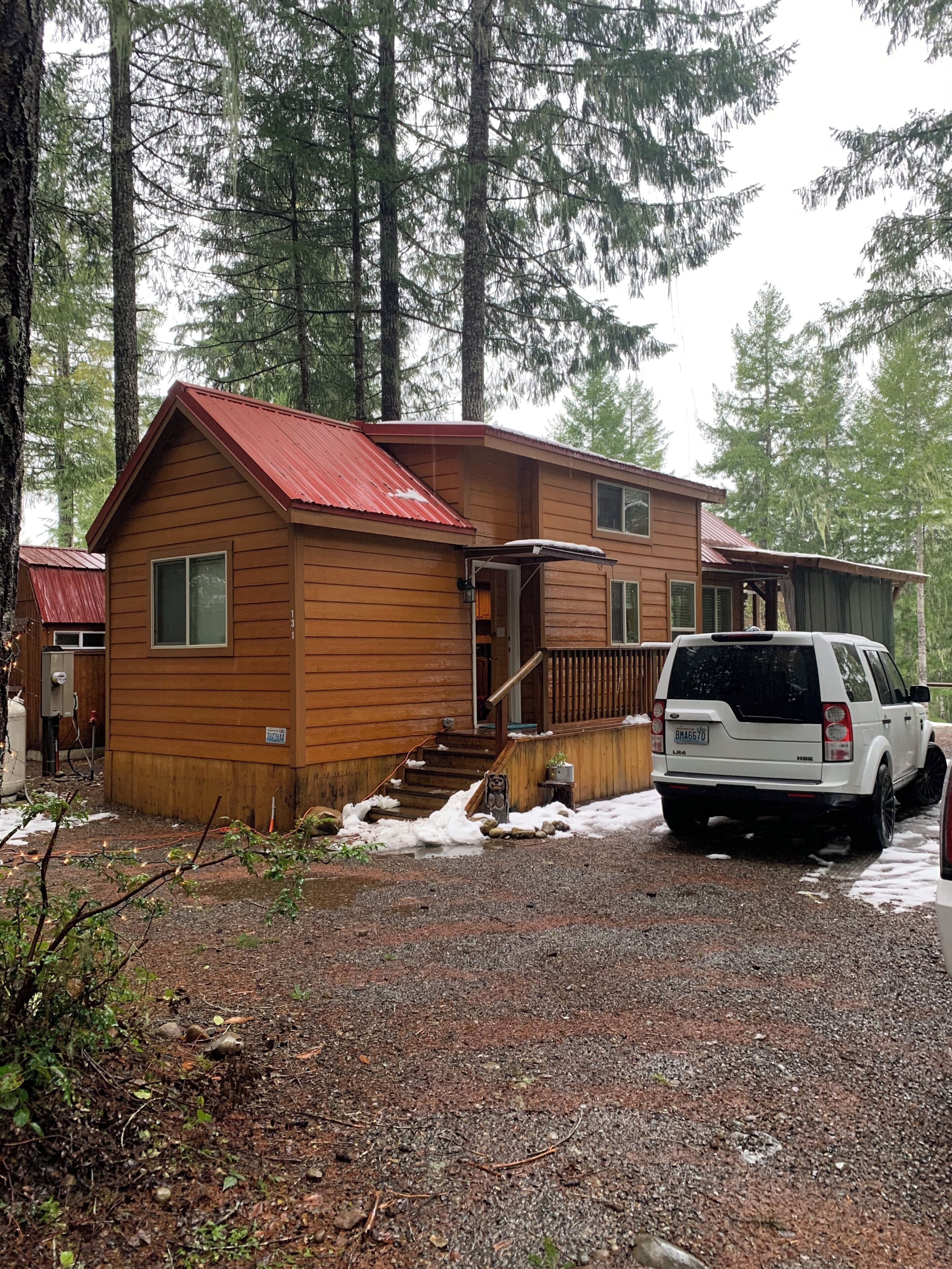 A cabin with a red roof, a covered porch, and a gravel driveway.