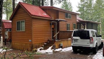 A cabin with a red roof, a covered porch, and a gravel driveway.