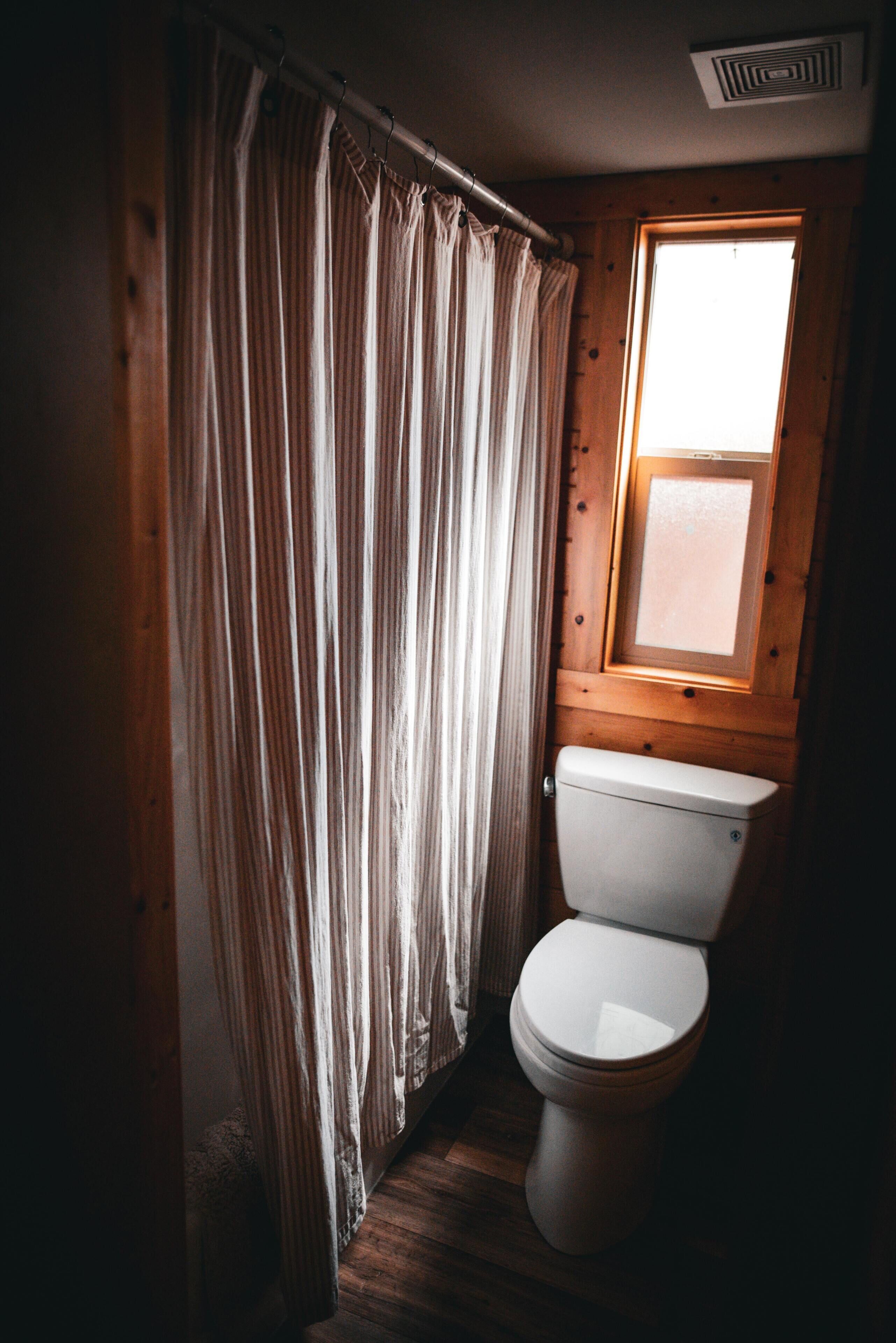 A small bathroom with a toilet, wooden walls, and a window.