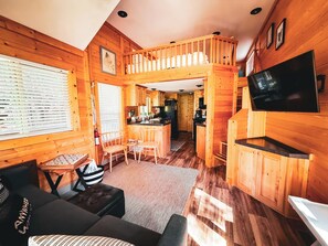 A cabin interior with a dining area, kitchen, and a living room with a sofa and chairs.