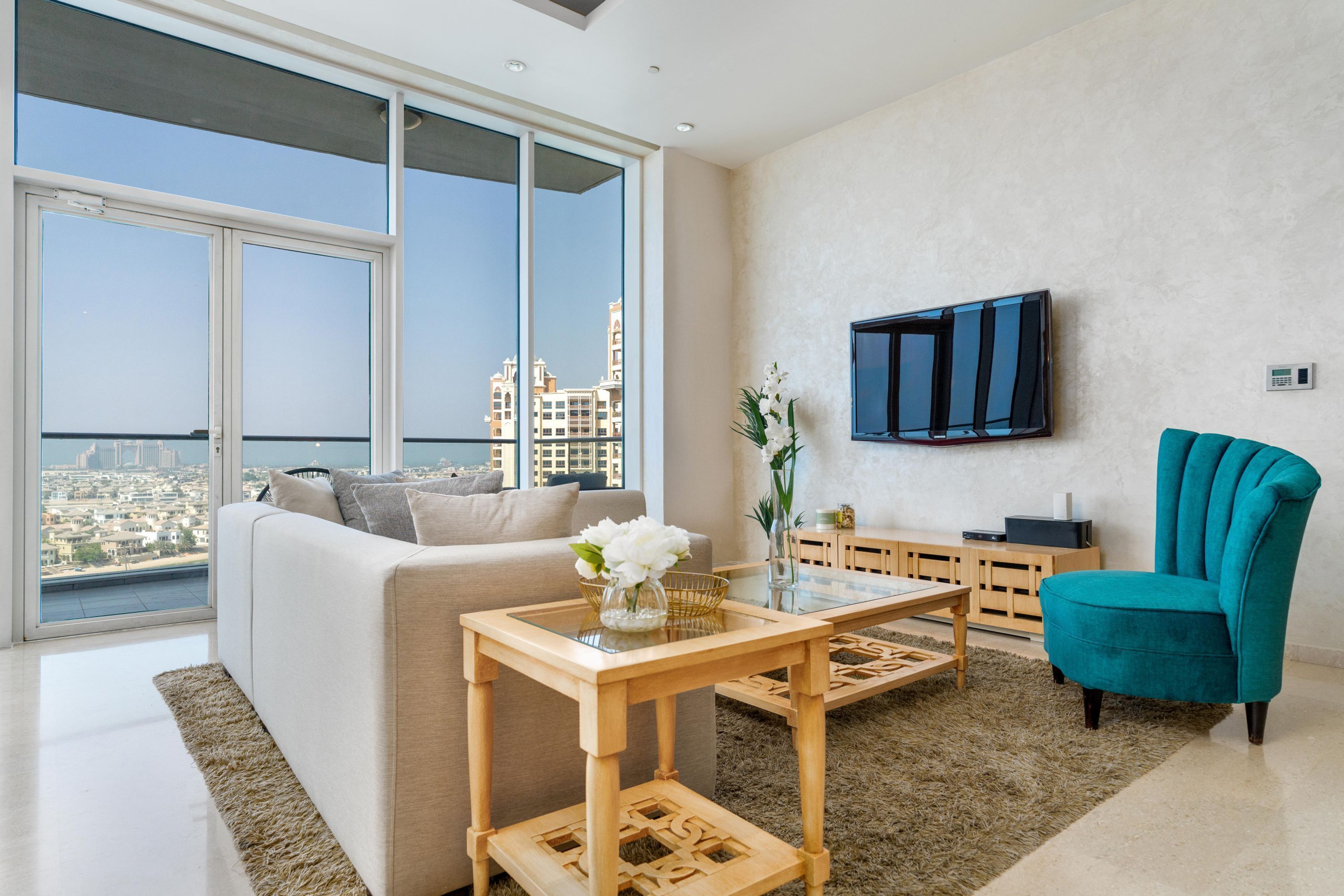 A modern living room with a sofa, a teal armchair, a coffee table, and a TV mounted on the wall.