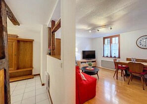 Una sala de estar con televisión, mesa de comedor y sofá rojo.