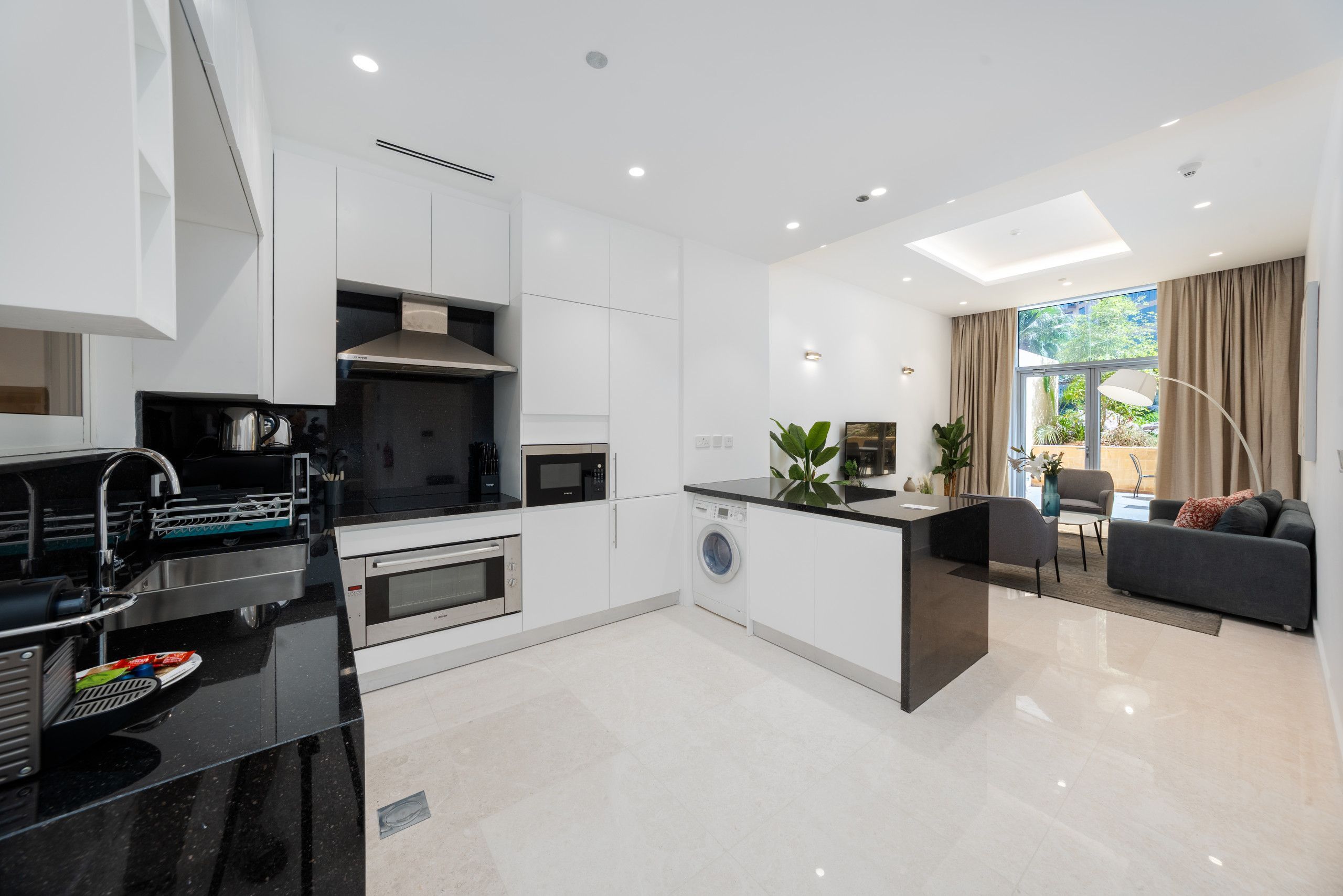 A modern kitchen with integrated appliances, a dining area with a sofa, and a view of the outdoors.