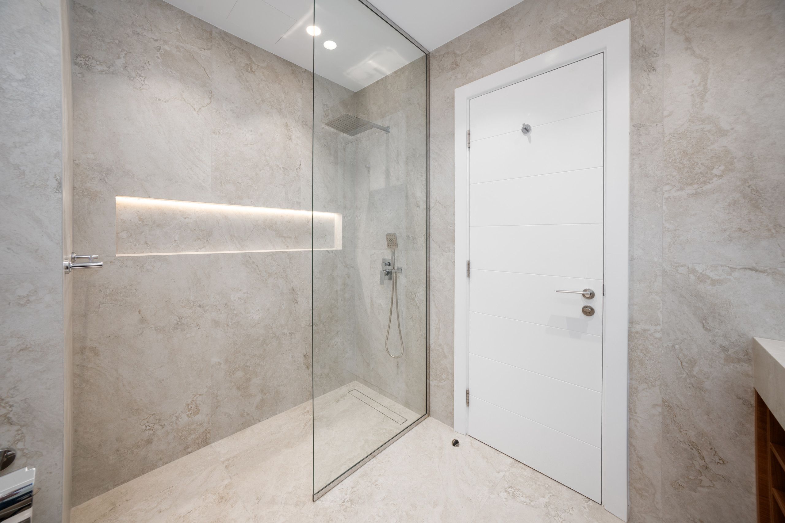 Une salle de bain moderne avec une douche à parois de verre, une porte blanche et un sol en marbre.