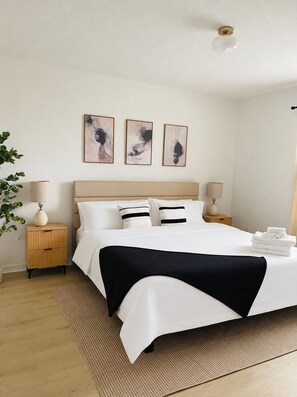 Habitación de hotel ordenada con una cama grande, lámparas de noche, una mesita de noche e iluminación en la pared.