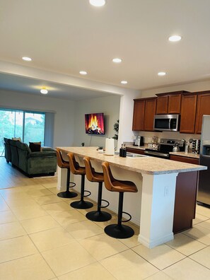 Una cocina moderna con una isla central, taburetes de bar, un televisor de pantalla plana y armarios de madera.