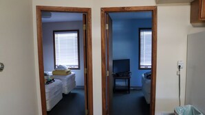 A hallway with a bed, a television, and a trash can. - Cozy Two-Bedroom Apartment at Sullivan Hills/Private Pond & 640 Acres to Explore (Lodgepole)