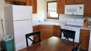 A kitchen with wooden cabinets, a white refrigerator, a microwave, a stove, a sink, and a dining table with chairs. - Cozy Two-Bedroom Apartment at Sullivan Hills/Private Pond & 640 Acres to Explore (Lodgepole)