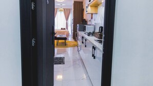 Un couloir mène à une chambre qui contient un lit, une petite table et une chaise. On y trouve également un coin cuisine équipé d’un four à micro-ondes, d’une cuisinière et d’un évier.