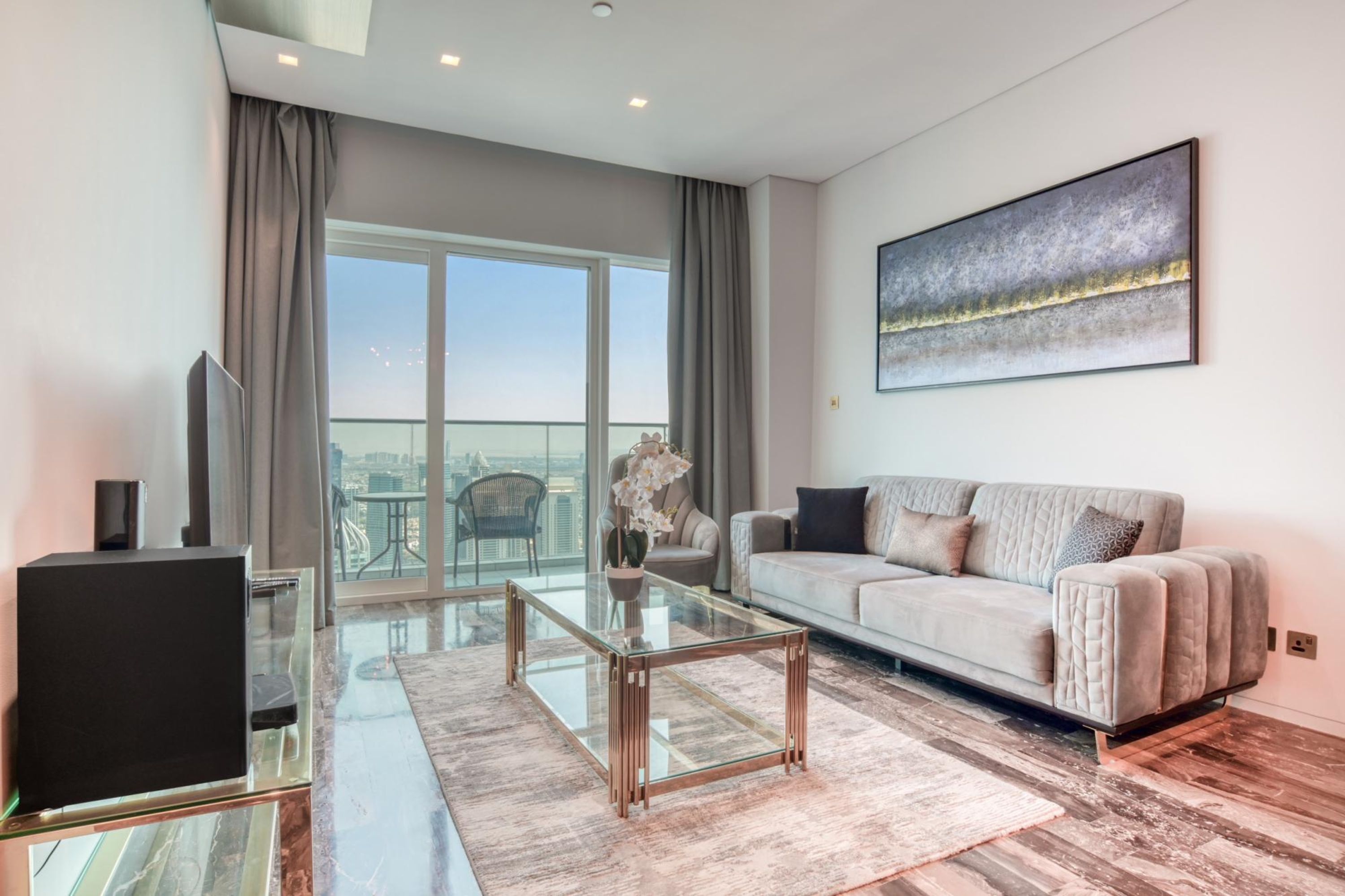 A modern living room with a glass coffee table, a sofa, a TV, and a large window with curtains.