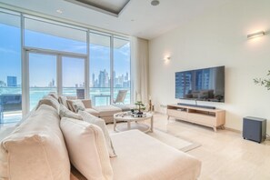 Una sala de estar moderna con un televisor grande, un sofá, una mesa de centro y vistas a un horizonte urbano a través de amplios ventanales.