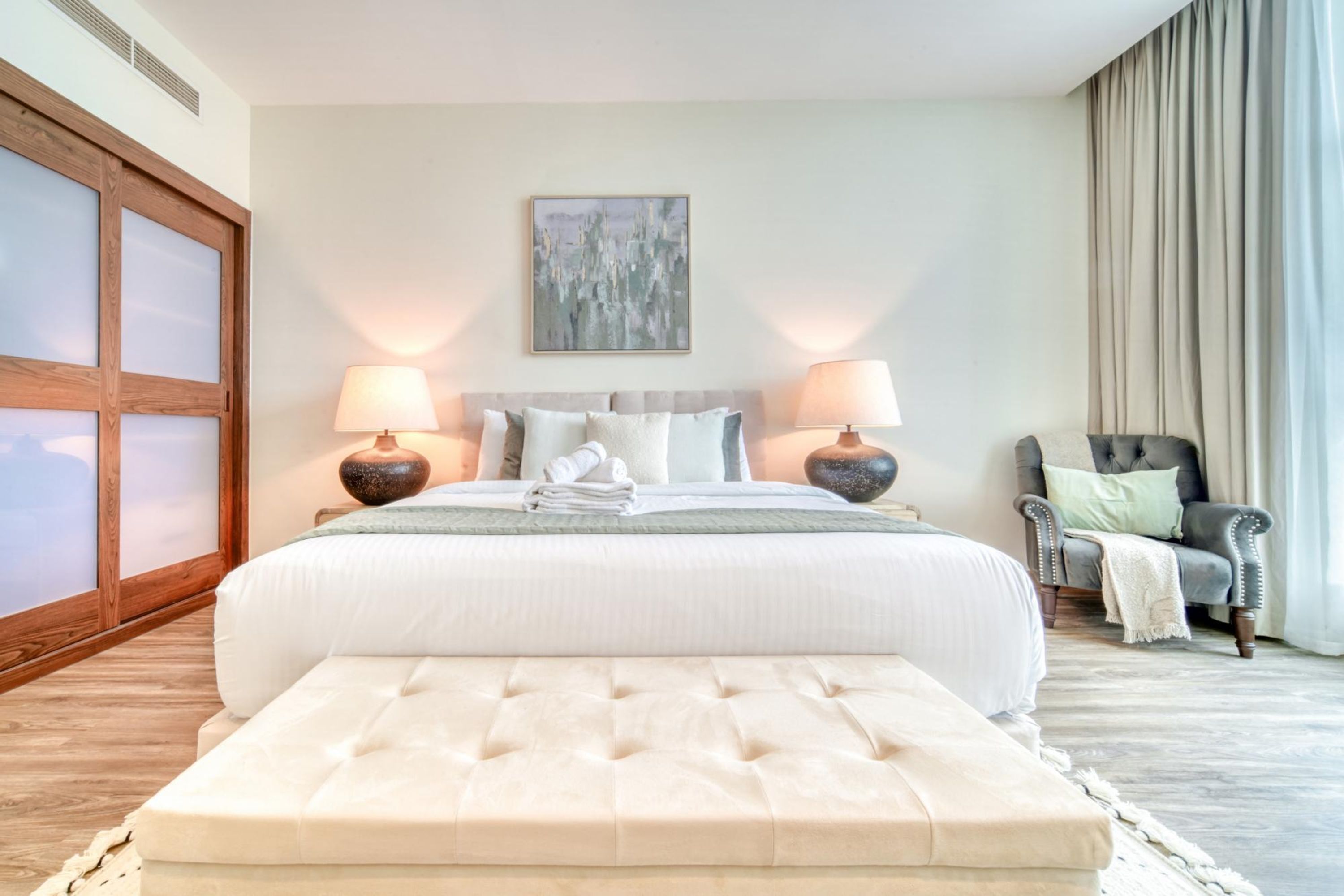 Een slaapkamer met een groot bed, twee bedlampen, een stoel en een schilderij aan de muur.