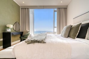 A bedroom with a large bed, a view of the sea, a desk with a chair, and a vase of flowers. - Sparkling Balcony Sea View Apt in Bluewaters (Dubai)