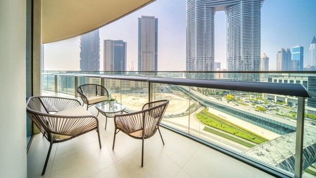 Ein Balkon mit Korbstühlen und einem Glastisch, mit Blick auf eine Skyline moderner Wolkenkratzer.