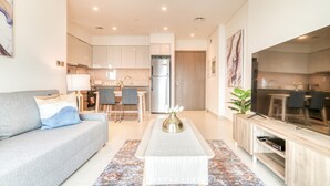 Ein modernes Wohnzimmer mit Sofa, Couchtisch, Fernseher und einer Küche im Hintergrund.
