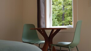 Une pièce comprenant un lit, une table avec deux chaises, une fenêtre donnant sur des arbres et un radiateur.