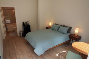 Un dormitorio con cama, mesitas de noche, una pequeña mesa y vistas al baño.