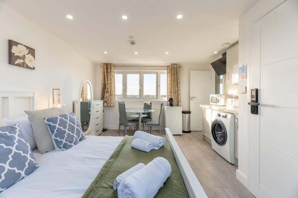 A hotel room with a bed, a desk, a chair, a washing machine, and a window with curtains.