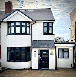 A two-story residential building with a dark blue front door, a small porch, and a chimney.