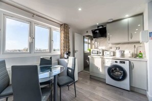 A compact kitchen with a washing machine, microwave, and a dining area with a table and chairs.