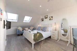 A bedroom with a bed, bedside tables, a vanity with a mirror, a sofa, and a window.