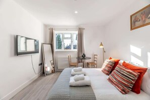 A hotel room with a bed, a TV, a window, a table with chairs, and a lamp. - Bright & Modern Studio Near London, EV Charger (Surrey)