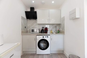 A compact laundry room with a washing machine, microwave, and cabinets.
