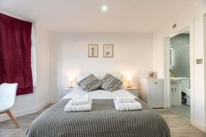 A neatly arranged bedroom with a bed, bedside tables, a chair, and a small refrigerator. - Studio with Access to Central London - EV charger (Surrey)