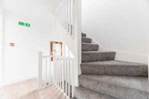 A staircase with grey carpeted steps and white railings, a fire exit sign, and a small red emergency exit sign.
