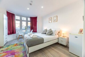 A modern bedroom with a bed, bedside tables, a nightstand, a window with curtains, and a colorful rug.