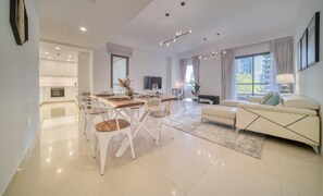 Ein modernes Wohnzimmer mit einer Couch, einem Essbereich mit Stühlen, einem Fernseher und einer Küche im Hintergrund.
