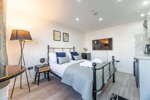 A modern bedroom with a bed, bedside tables, a lamp, a TV, and a kitchenette.