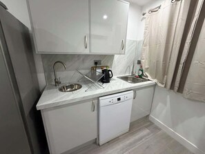 A compact kitchen with white cabinets, a dishwasher, a sink, and a kettle.