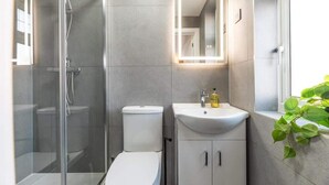 Ein modernes Badezimmer mit einer gläsernen Duschkabine, einer weißen Toilette, einem Waschbecken mit Spiegel und einer Topfpflanze.