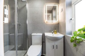 A modern bathroom with a glass-enclosed shower, a white toilet, a sink with a mirror, and a potted plant.